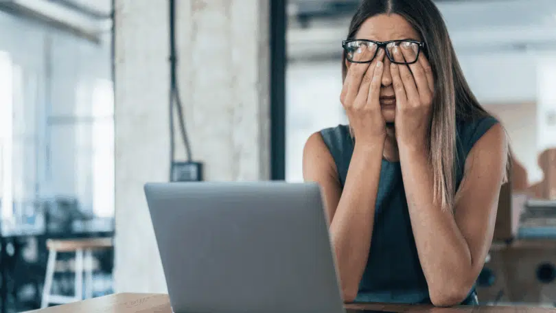 Mulher com as mãos no rosto diante de um notebook em um escritório