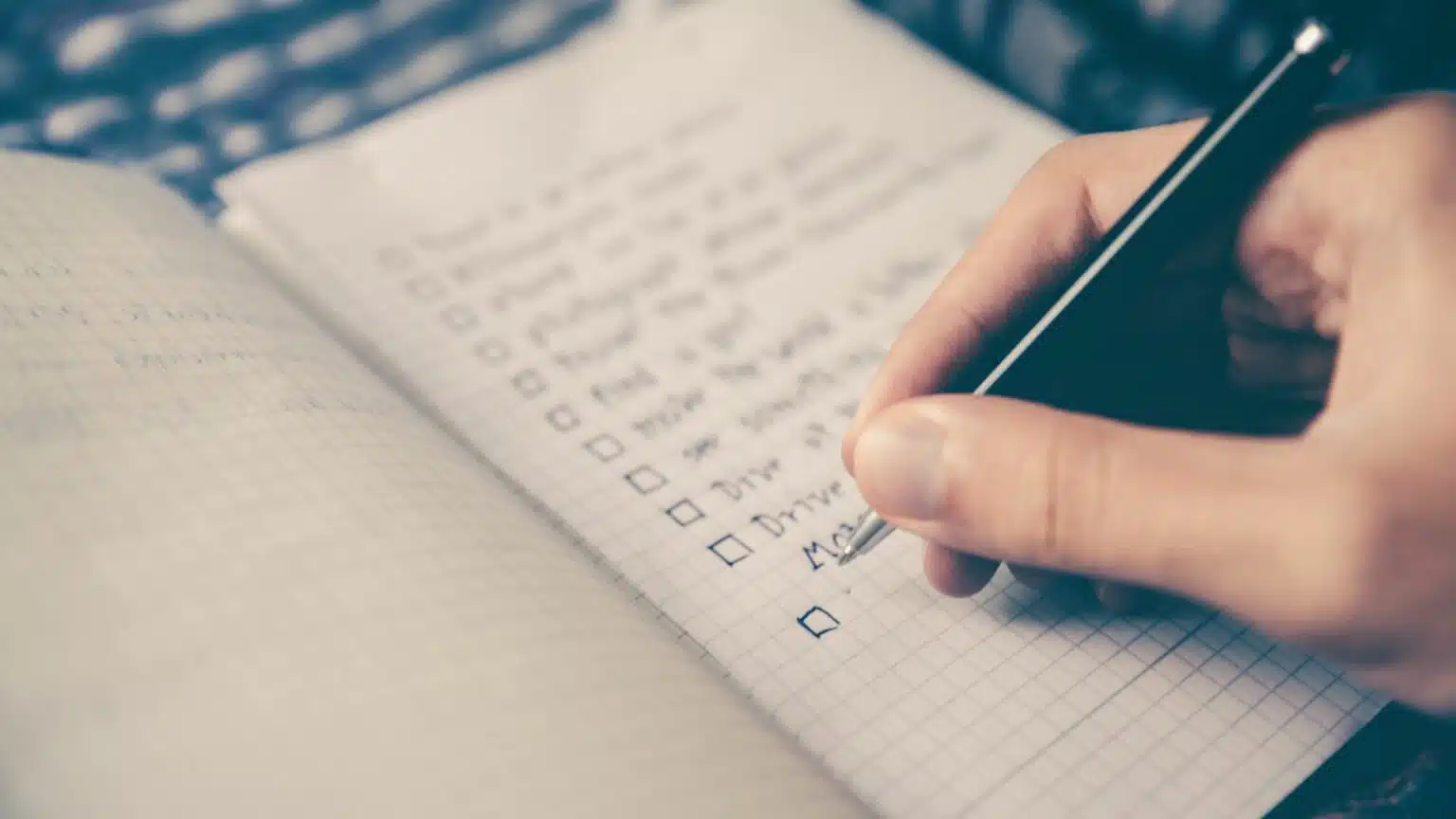 Mão anotando uma lista de itens em um caderno quadriculado