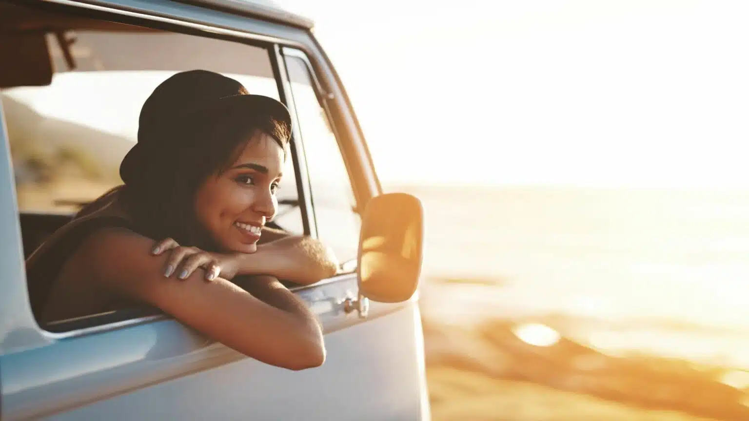 Mulher sorridente apoiada na janela de uma van ao pôr do sol